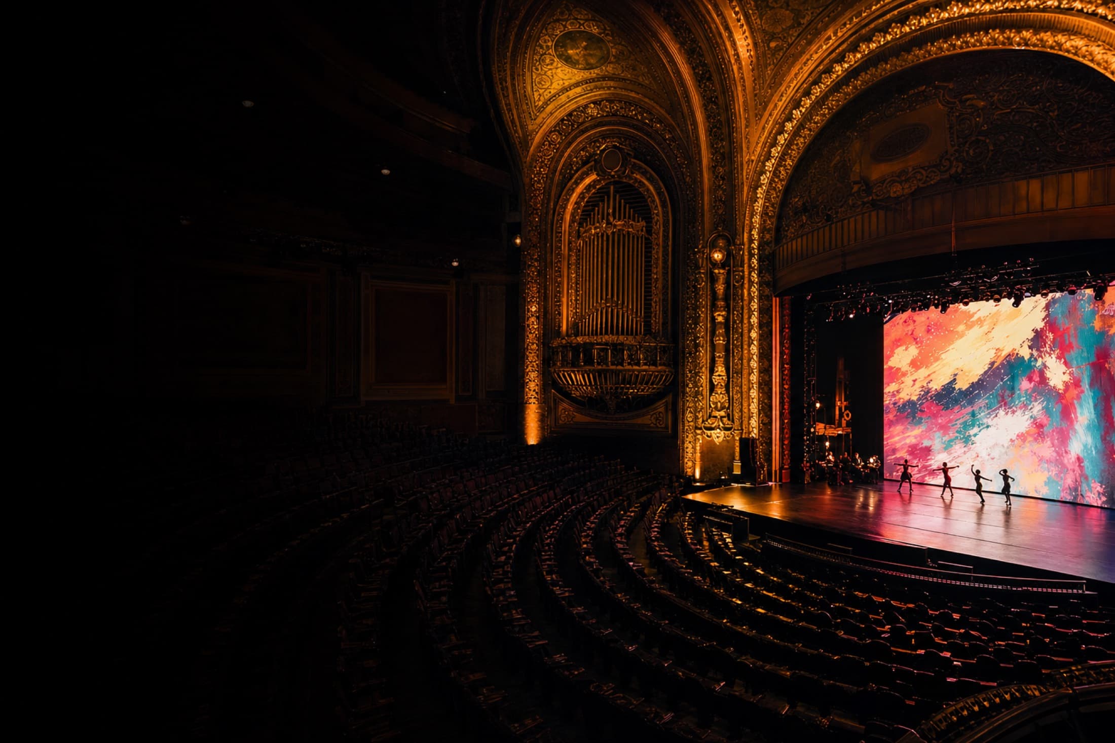Inside the Coliseum of Art. The 1916 Coliseum Theatre filled with contemporary installations: a 30-foot LED wall, lasers crossing the room, neon ceiling sculptures, and large abstract paintings flanking the historic ornate plaster