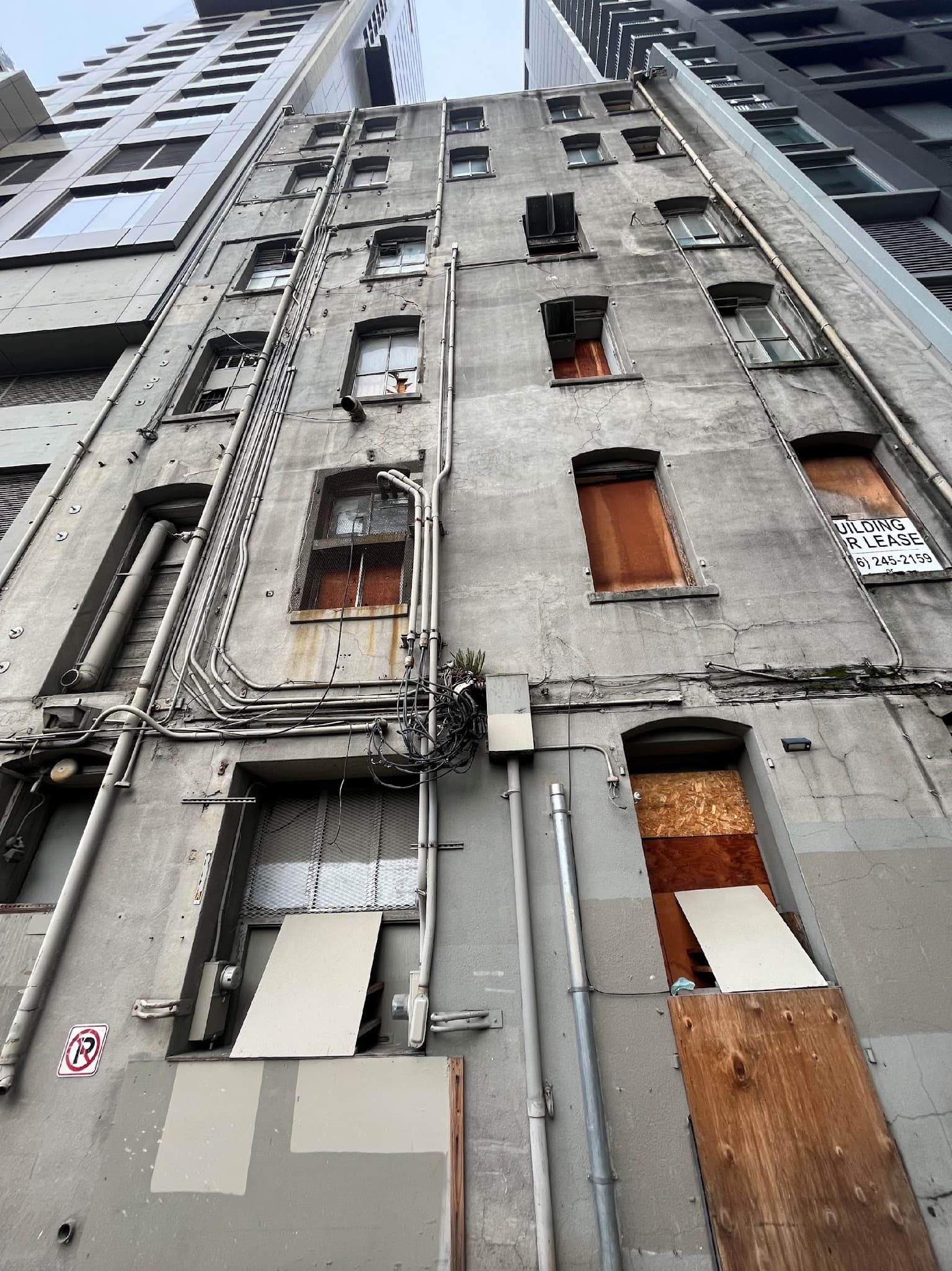 The back of the Lusty Lady building from the alley: weathered concrete walls, plywood-covered windows, conduit and HVAC, a 'Building For Lease' sign at the top